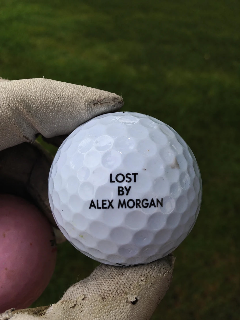 A golf ball held in a glove with the message Lost by Alex Morgan