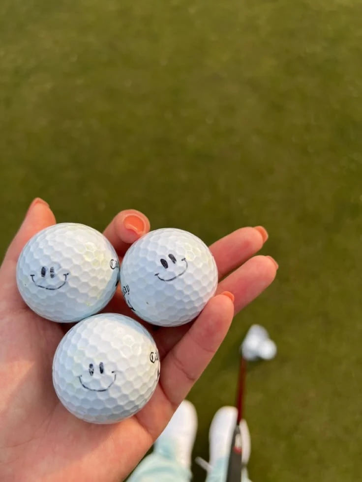 Three golf balls with small smile designs resting in a hand