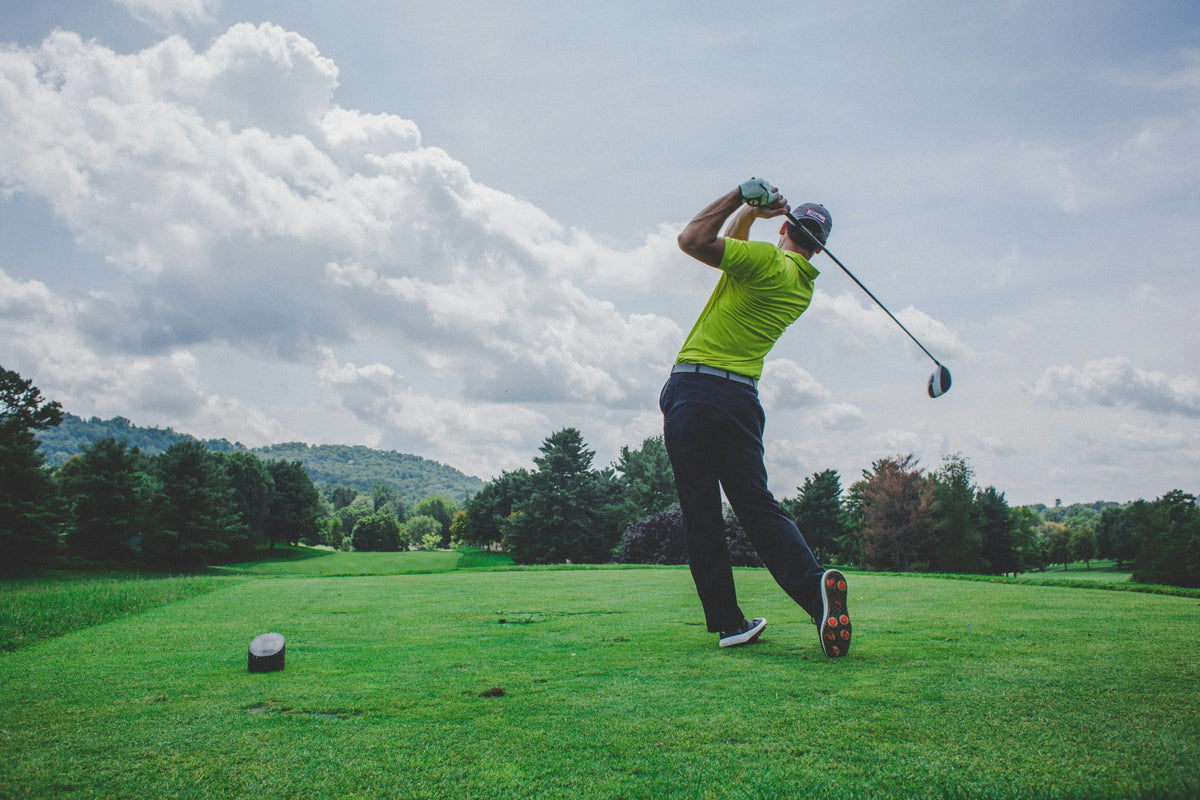 Golfer finishing a swing on a green fairway beneath a clouded sky